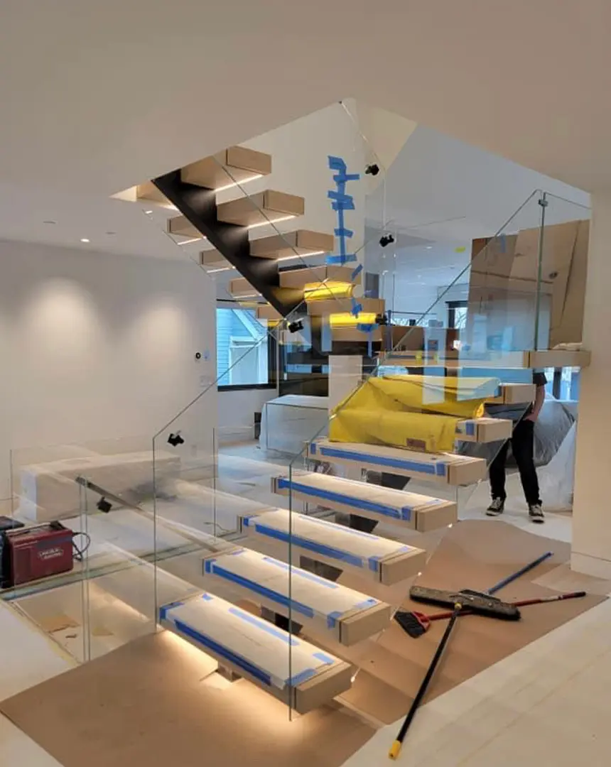Frameless glass railing panels being installed along a floating staircase
