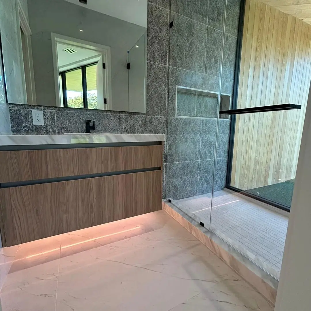 Modern walk-in shower with a fixed glass panel, patterned gray tile and marble curb