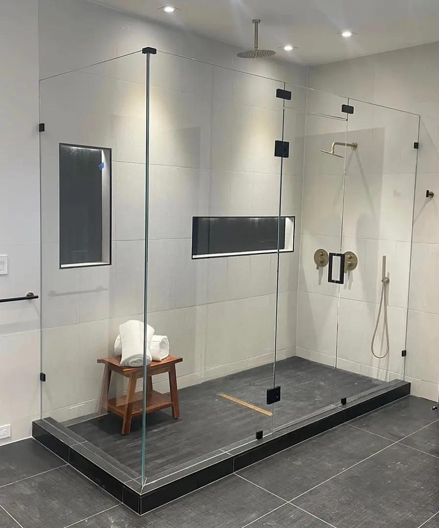 Full-height frameless glass steam shower enclosure with matte black clamps and brass fixtures